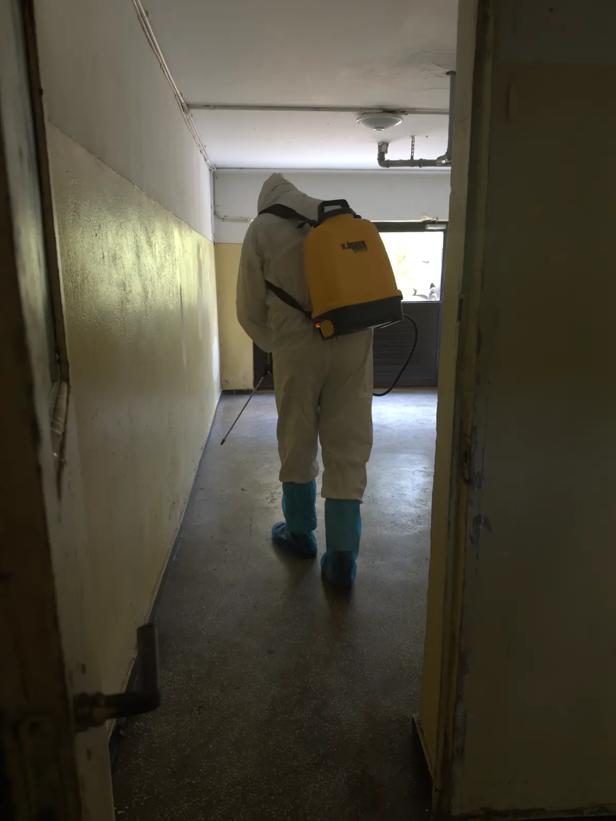 Tehnician DDD cu pulverizator profesional pe spate, în combinezon și cizme de protecție